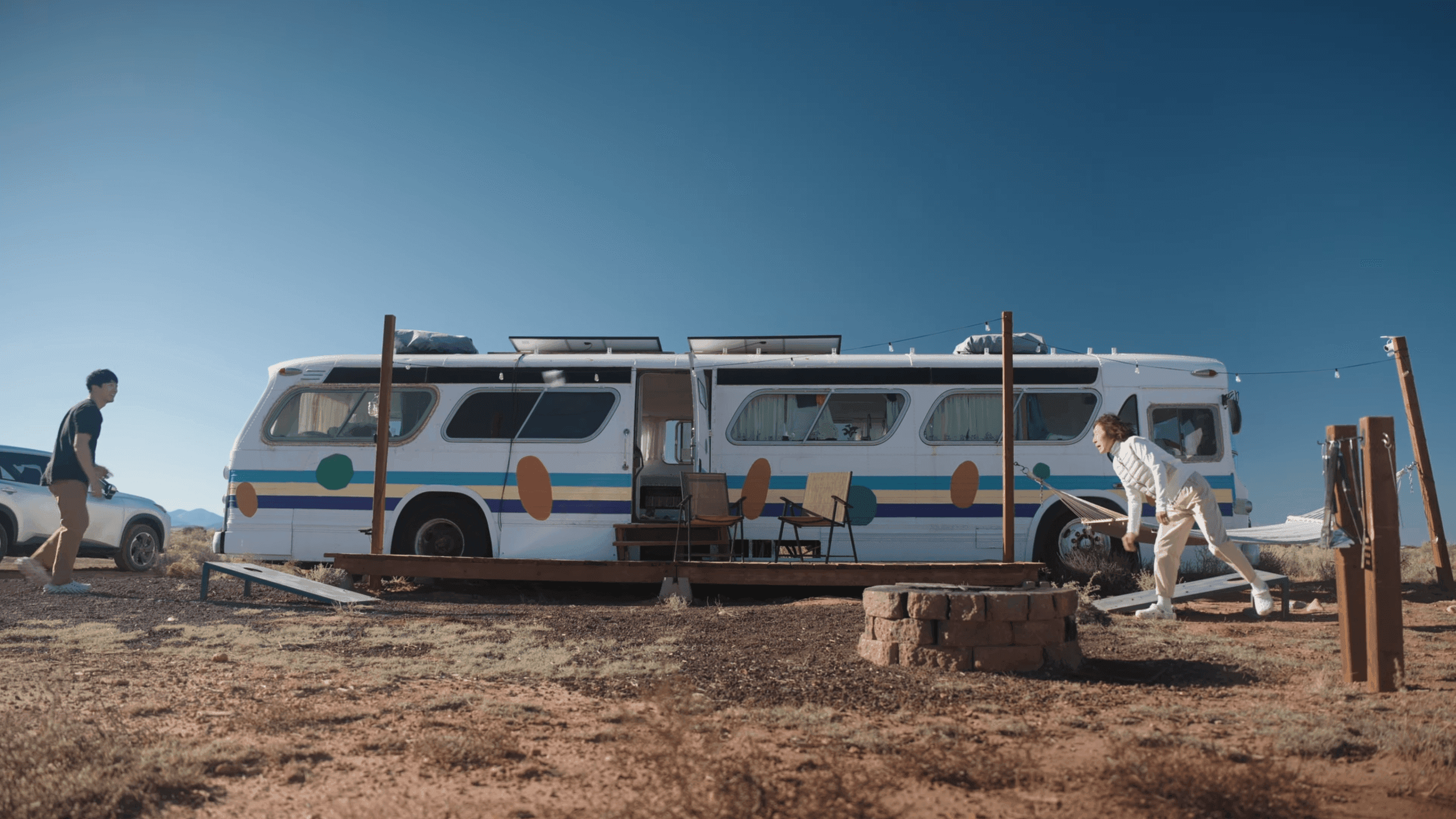Road trip camp in the desert: a painted vintage bus, a fire pit, and a game of cornhole